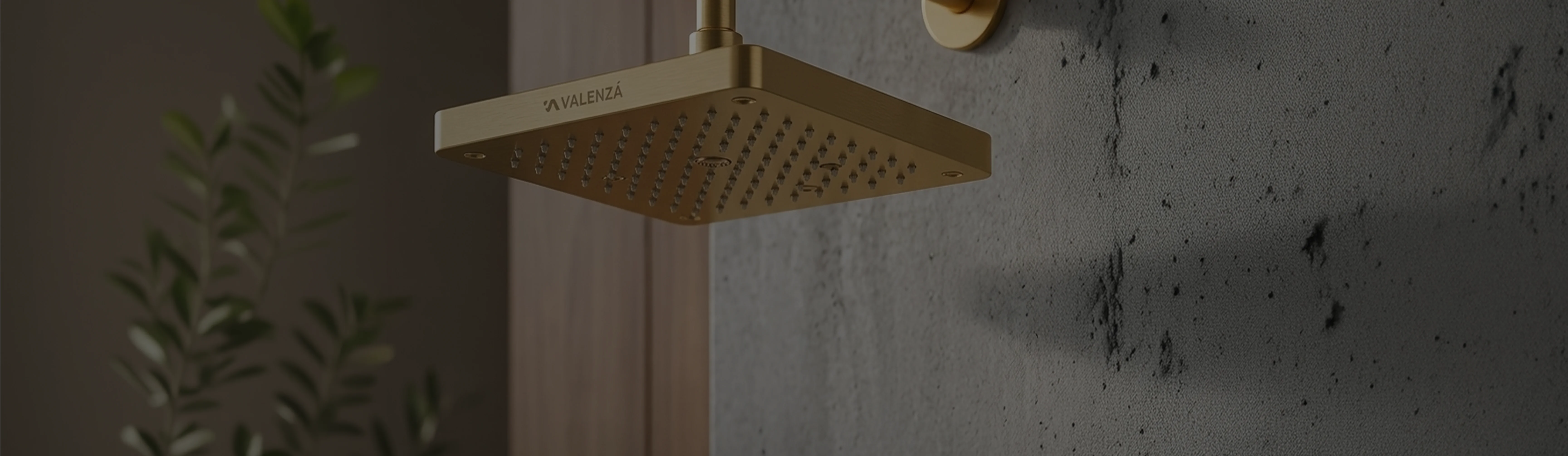 Brushed gold Valenzá rain shower head on textured dark stone wall