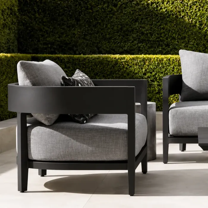 Outdoor armchair with a black aluminium frame and grey cushions in front of a clipped hedge