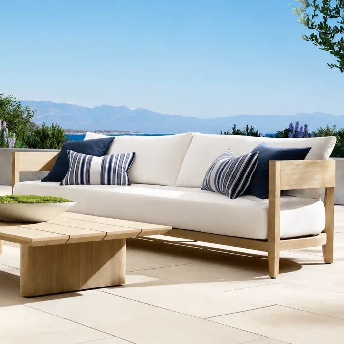 Bleached oak outdoor sofa with white cushions and navy striped pillows facing the sea