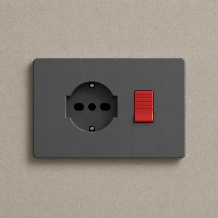 Graphite plate with a round Schuko socket and a red rocker switch on a sand coloured wall