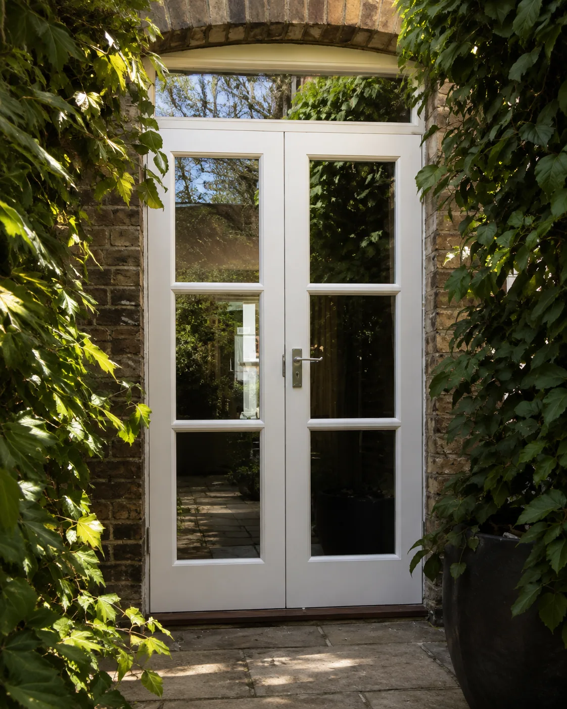 White glazed double door in a brick arch leading to a planted courtyard